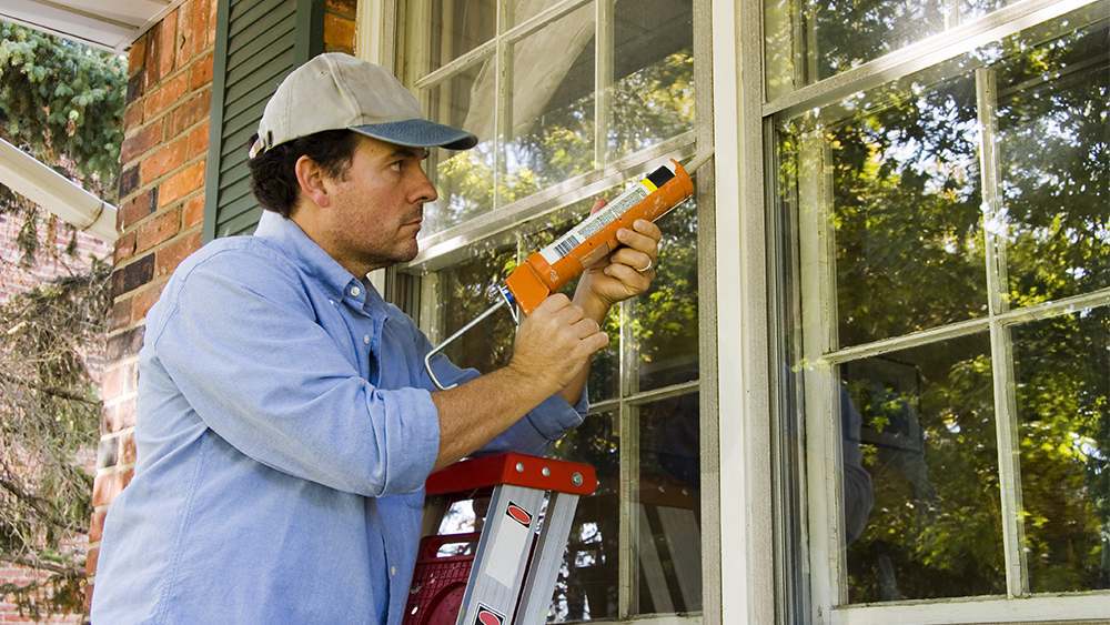 A man insulating a window with caulk